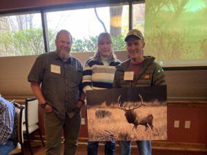 Three people holding a photo of an elk.
