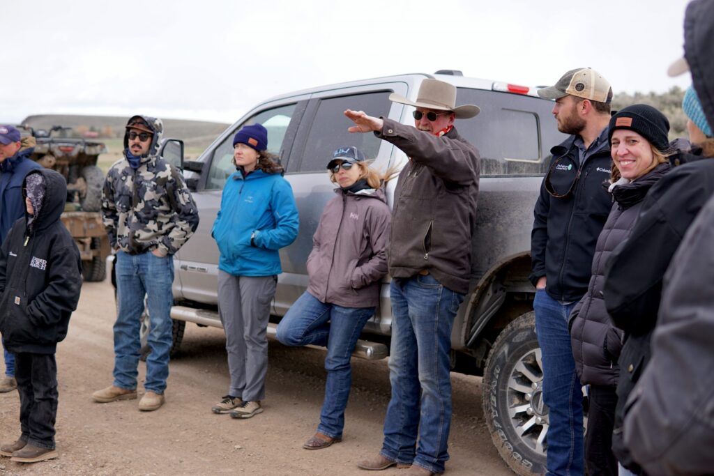 A crowd of people lean against a pickup truck and look out into the landscape.