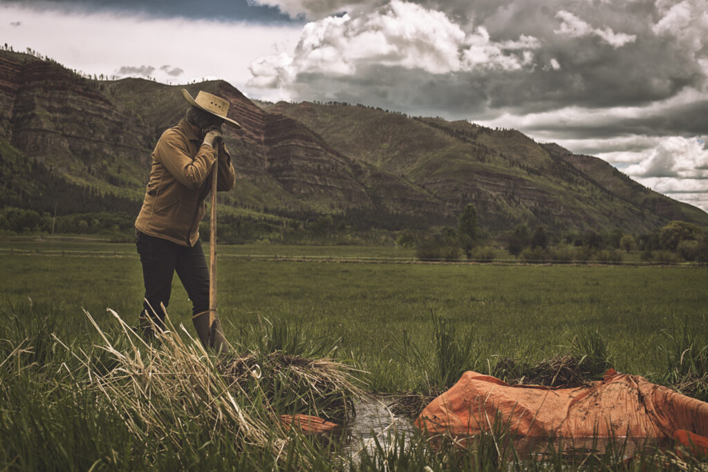 A rancher rests on a shovel near an irrigation ditch.