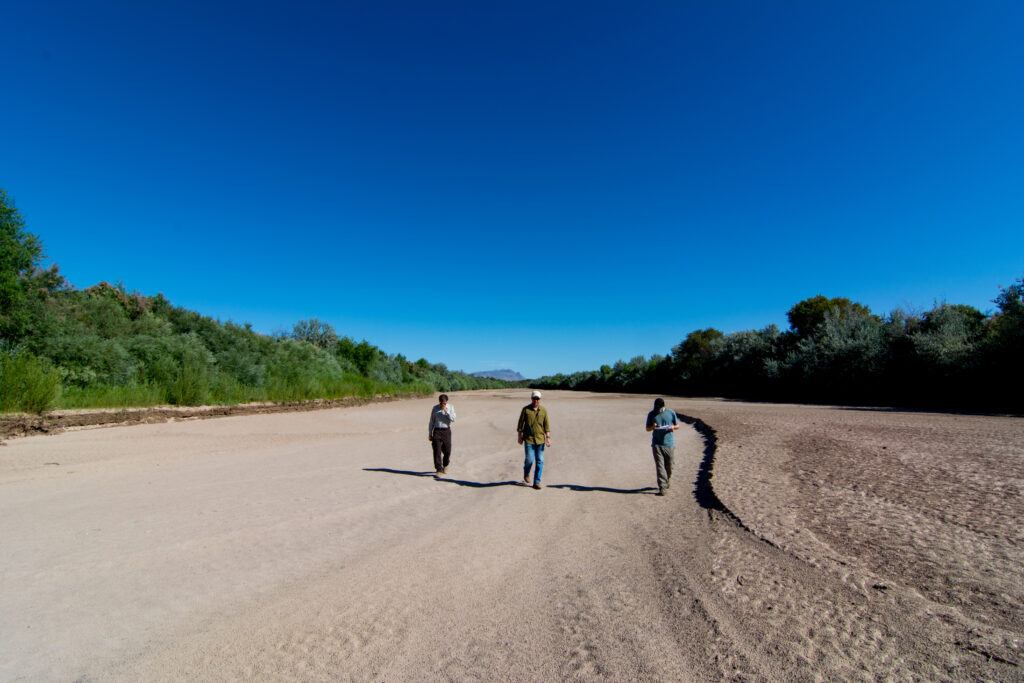 Three people walk in a dry riverbed.
