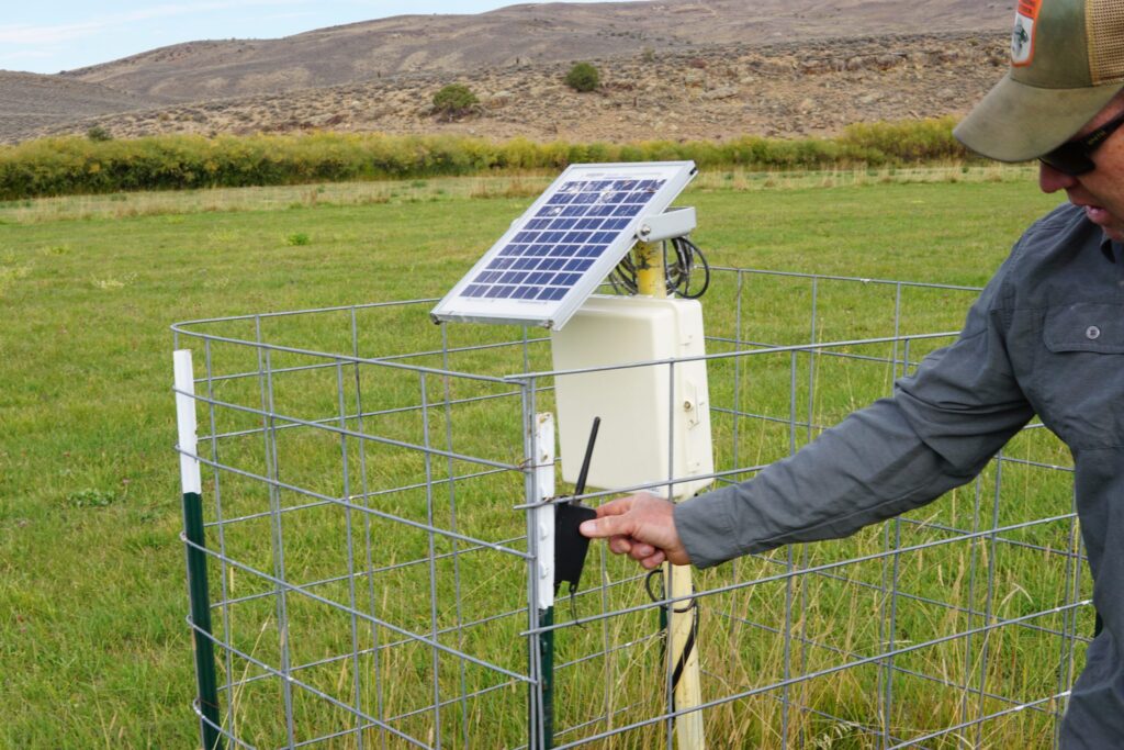 An arm reaching through a fence to adjust a solar paneled control site.