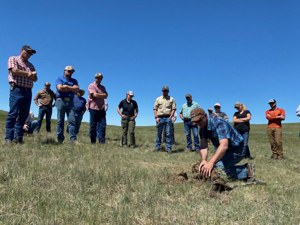 A group of people watches a man turn over a clump of sod.