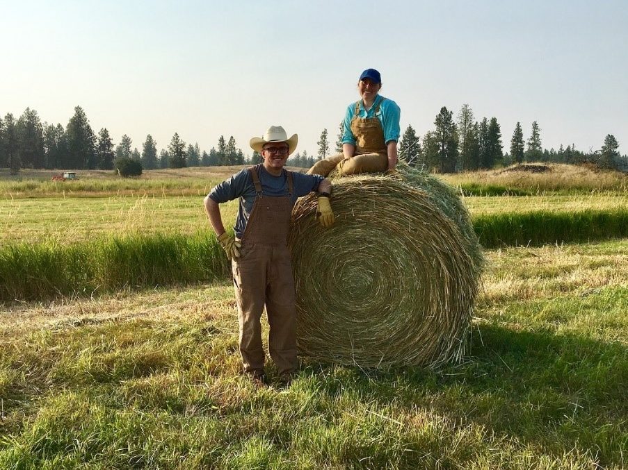 Two people pose on a bale of hay.