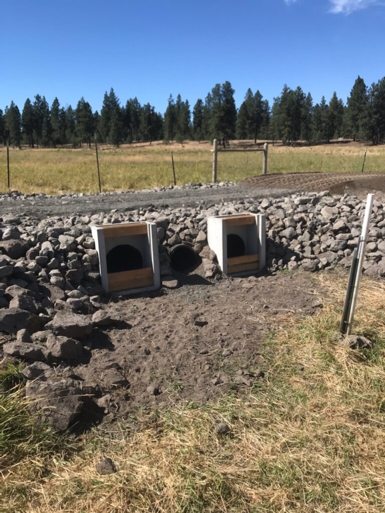 A road passes over large rocks and three new culverts in a dry ditch.