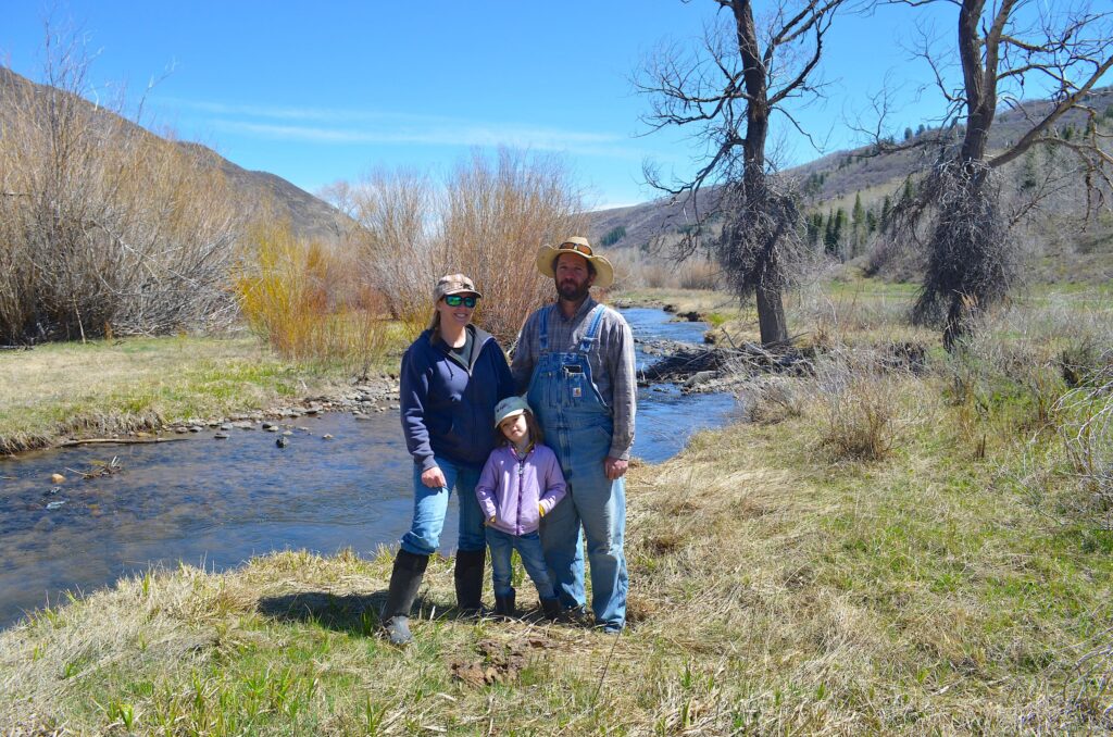 Two adults and a child stand by a streambank.