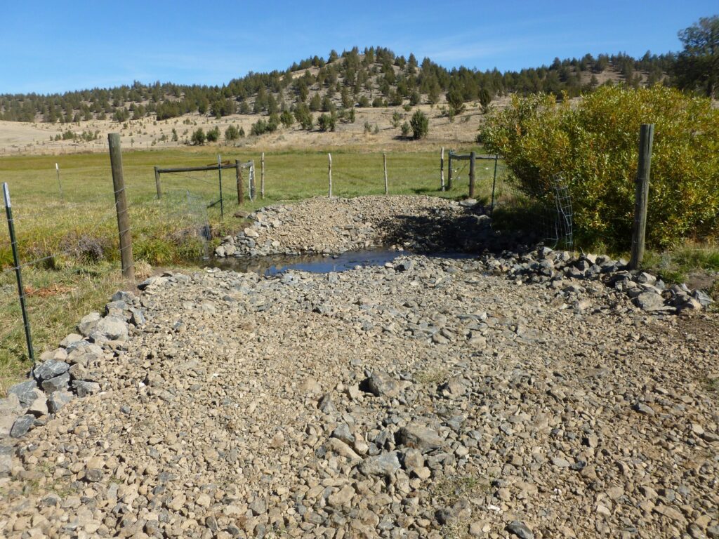 Gravel runs through a creek surrounded by fencing.