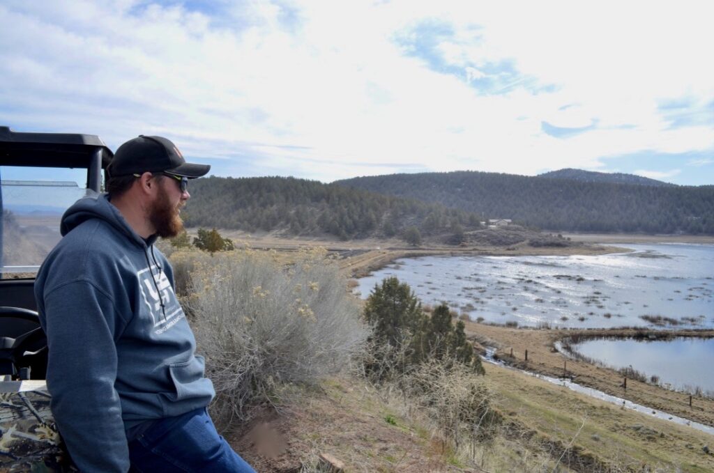 A man leans on a side by side and looks out at fields converted into wetlands from a hilltop.