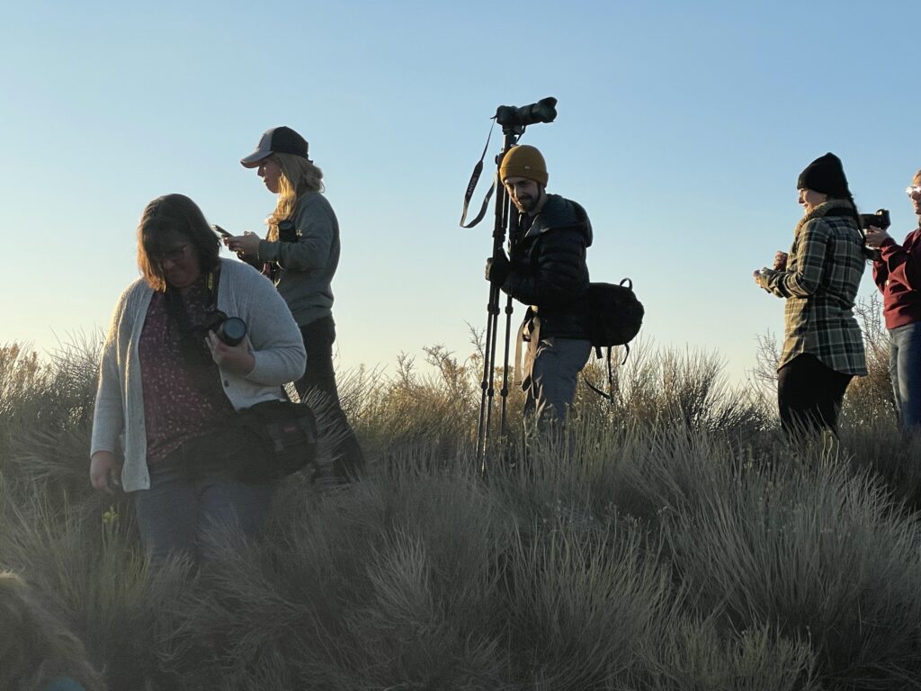 People gather on a hill top at dawn with camera gear and other storytelling equipment.