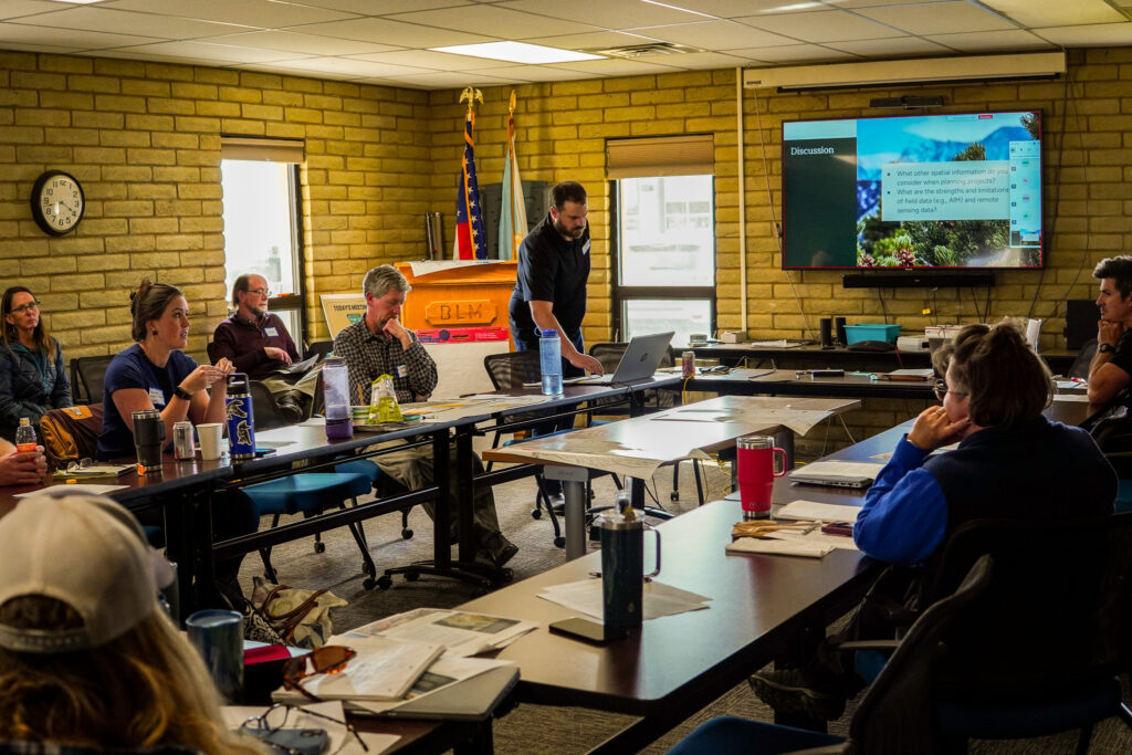 A group of people sitting in a conference room viewing a slideshow during a technical transfer workshop.